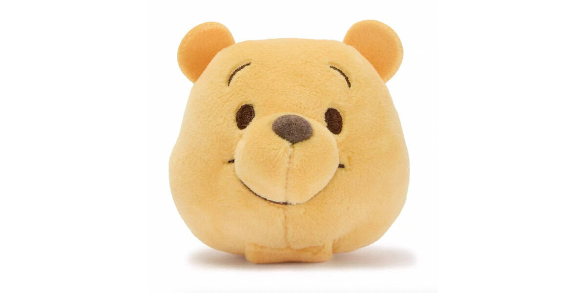 A plush toy shaped like the head of Winnie the Pooh, featuring a round yellow face, small brown nose, embroidered smile, and two round ears.
