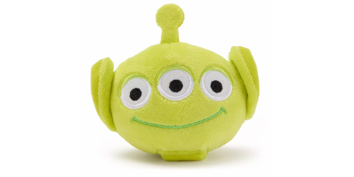 A plush toy shaped like a green, three-eyed alien with a smiling face, large ears, and a small antenna on top. The toy is soft and round, resembling a character from the Toy Story franchise.