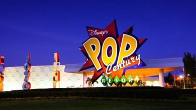 The entrance of Disney’s Pop Century Resort at night, featuring a brightly lit, colorful sign with bold letters and playful design elements against a deep blue sky.