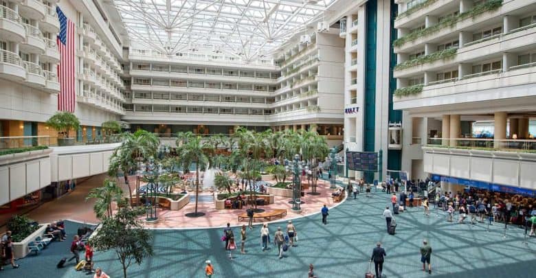 Spacious Orlando Airport atrium lined with palms, families heading to Disney fun, and a bold American flag welcoming visitors.