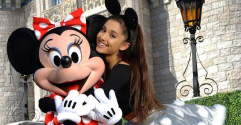 Ariana Grande wearing Minnie Mouse ears shares a joyful hug with Minnie Mouse in front of Cinderella Castle at Disney World.