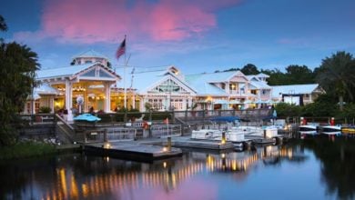 Lakeside hotel restaurant with boats, twinkling lights, and a pink Disney sunset reflected on the water—pure park enchantment.