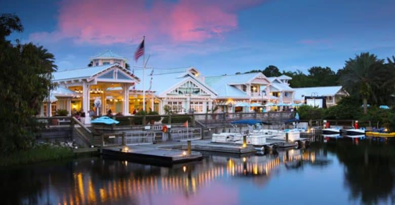 Lakeside hotel restaurant with boats, twinkling lights, and a pink Disney sunset reflected on the water—pure park enchantment.