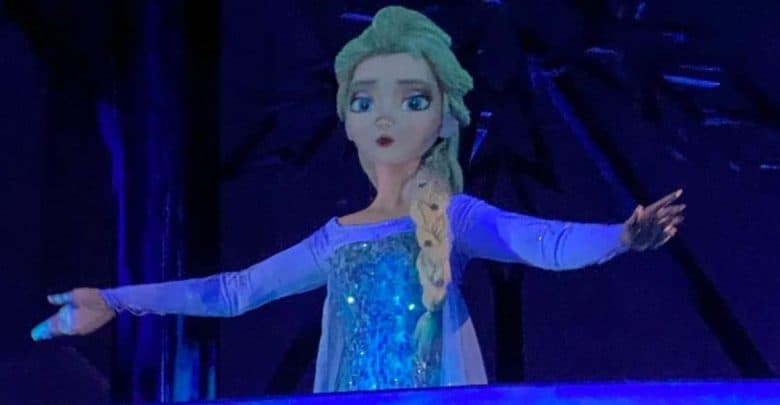 Elsa in her blue dress stands center stage, arms wide, bringing Frozen magic to life for fans at a dazzling Disney parks show.
