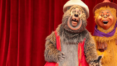 Big Al and Liver Lips McGrowl smile in their signature hats and vests before red curtains, capturing Frontierland’s whimsy.
