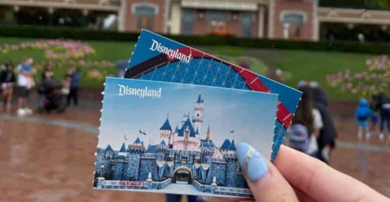 Two permanent Disneyland tickets held up at the iconic entrance gates, ready for a magical day at the park.