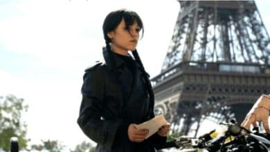 A mysterious woman in a sleek black coat poses with a letter in hand near the iconic Eiffel Tower, while an outstretched arm from the side adds an air of suspense—like a live-action scene you’d find at Universal Studios’ thrilling Netflix experience or a Wednesday-themed attraction, blending cinematic excitement with theme park magic.