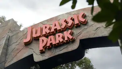 Jurassic Park entrance arch with bold red logo, surrounded by lush trees and dramatic clouds, welcoming guests into the thrilling Universal Studios adventure.