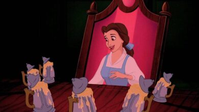 Belle looking into a mirror with mugs on a table in front of her.