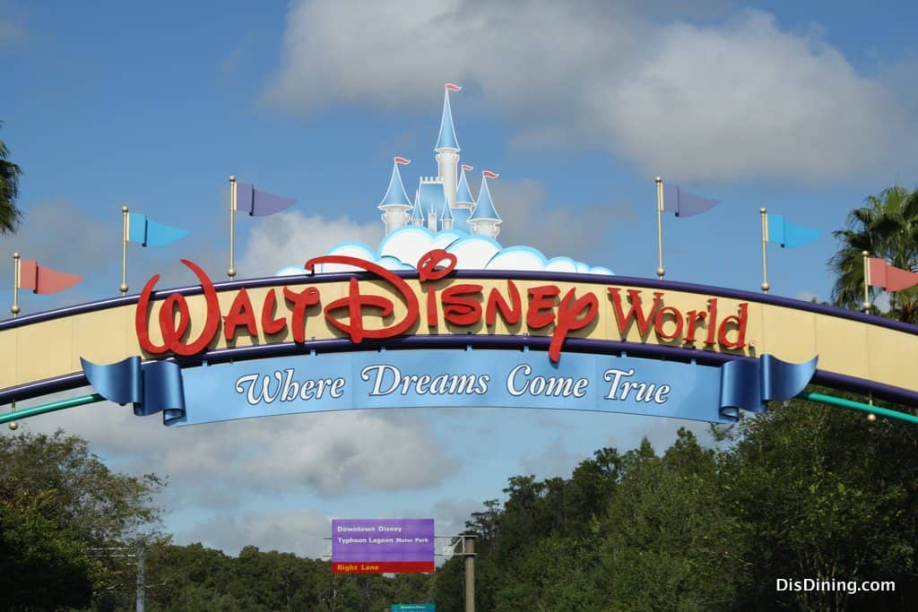 Walt Disney World entrance sign with a castle and "Where Dreams Come True" slogan under a blue sky, welcoming fans to the magic.