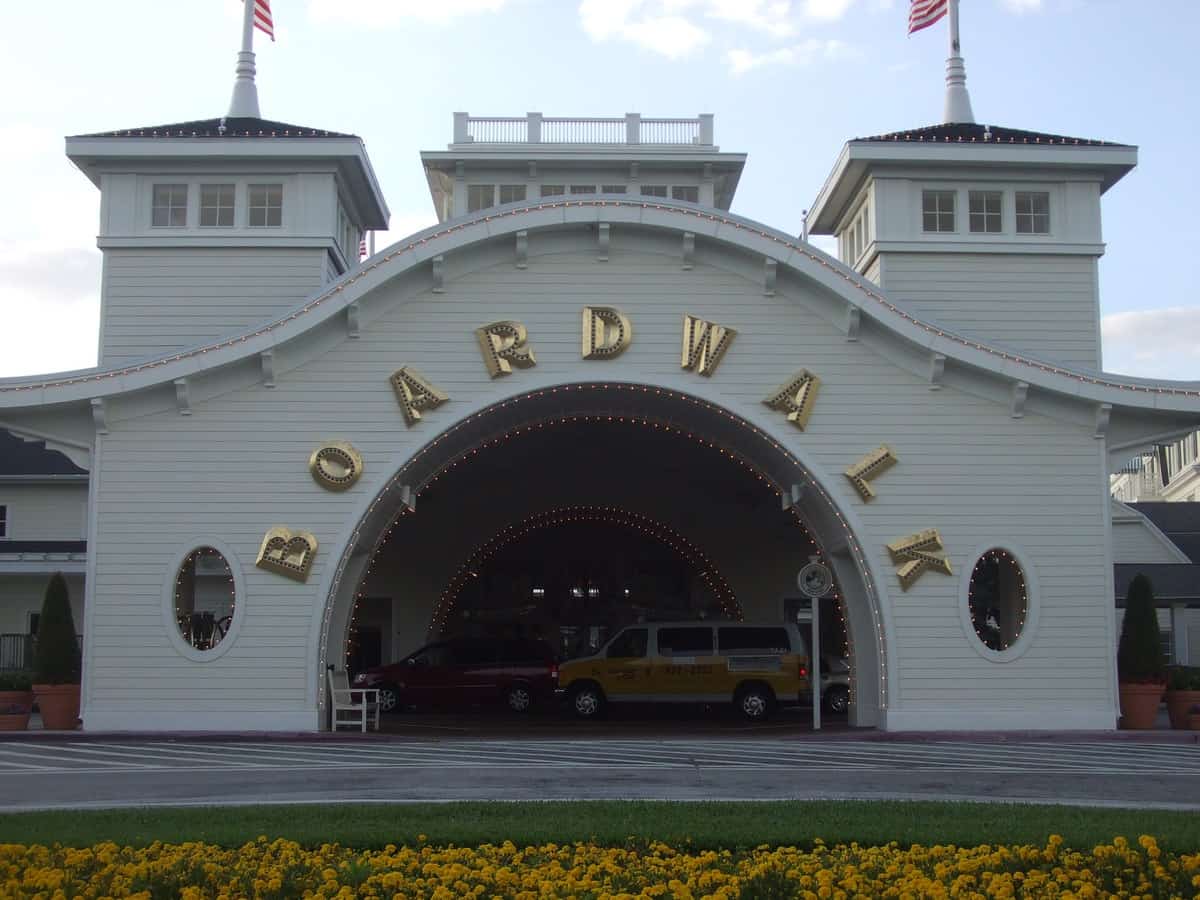 Disney’s BoardWalk entrance with signature gold arch, parked cars, and bright flowers—steps from all the excitement near EPCOT.