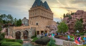 Guests stroll past a picturesque stone building and vibrant rose gardens at Disney World, soaking in the magical sunset ambiance.