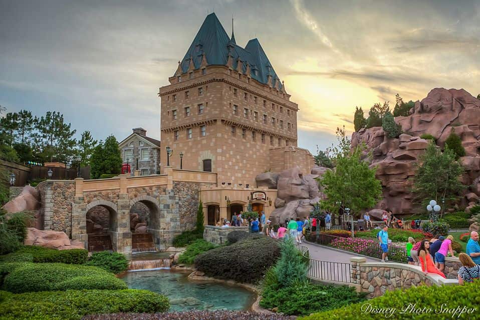 Guests stroll past a picturesque stone building and vibrant rose gardens at Disney World, soaking in the magical sunset ambiance.