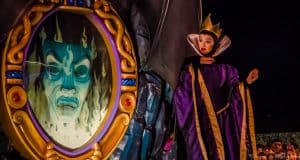 The Evil Queen greets guests beside her glowing magic mirror, where the Spirit’s green face appears during the Disney Parks show.