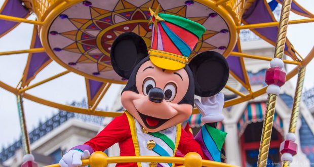 Mickey Mouse greets fans, waving in a dazzling parade uniform from a vibrant, gold-trimmed float at Walt Disney World.