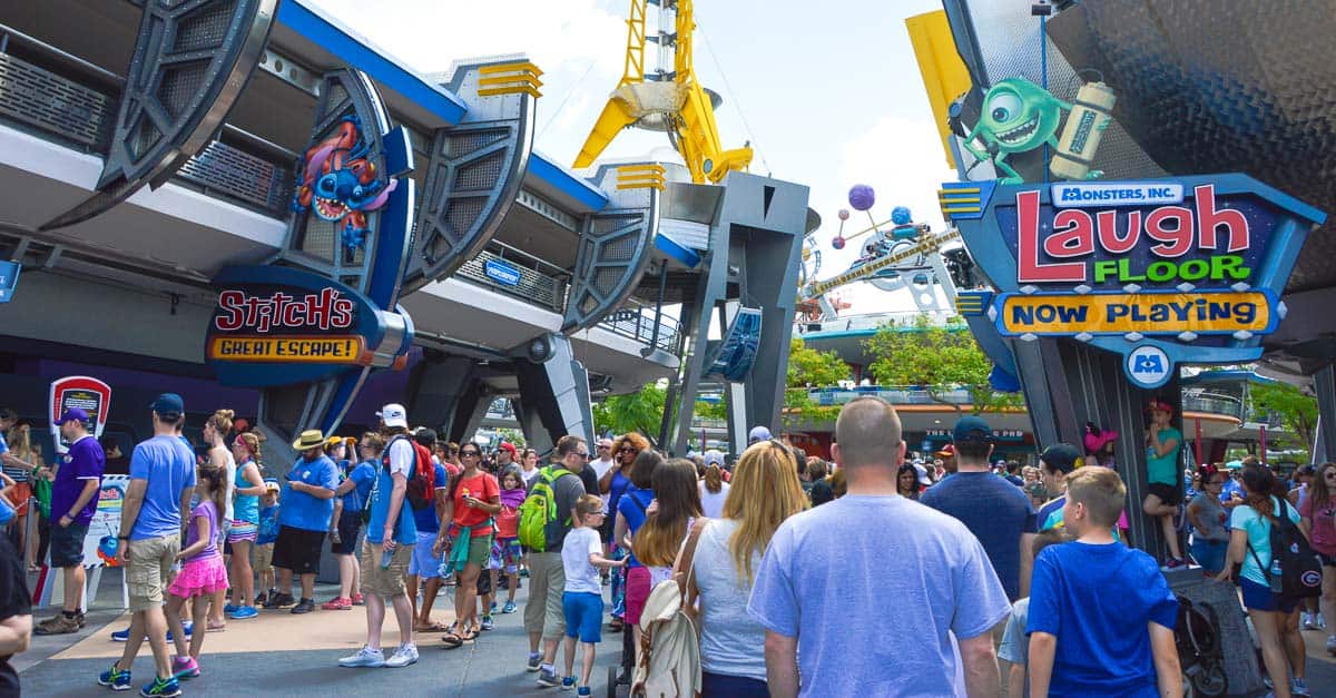 Guests explore Tomorrowland at Disney World, passing Stitch's Great Escape and Monsters, Inc. Laugh Floor attractions.