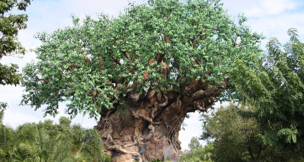 The Tree of Life, adorned with intricate animal carvings, rises above Animal Kingdom’s lush landscape under a vibrant blue sky.