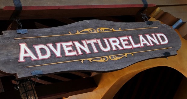 The iconic Adventureland entrance sign welcomes guests to thrilling attractions with bold white lettering on natural wood.
