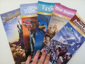 A fan showing off vibrant nails holds five Disney World park maps, ready for adventure across Magic Kingdom, EPCOT, Studios & Animal Kingdom.