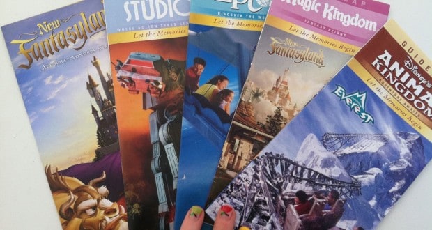 A fan showing off vibrant nails holds five Disney World park maps, ready for adventure across Magic Kingdom, EPCOT, Studios & Animal Kingdom.