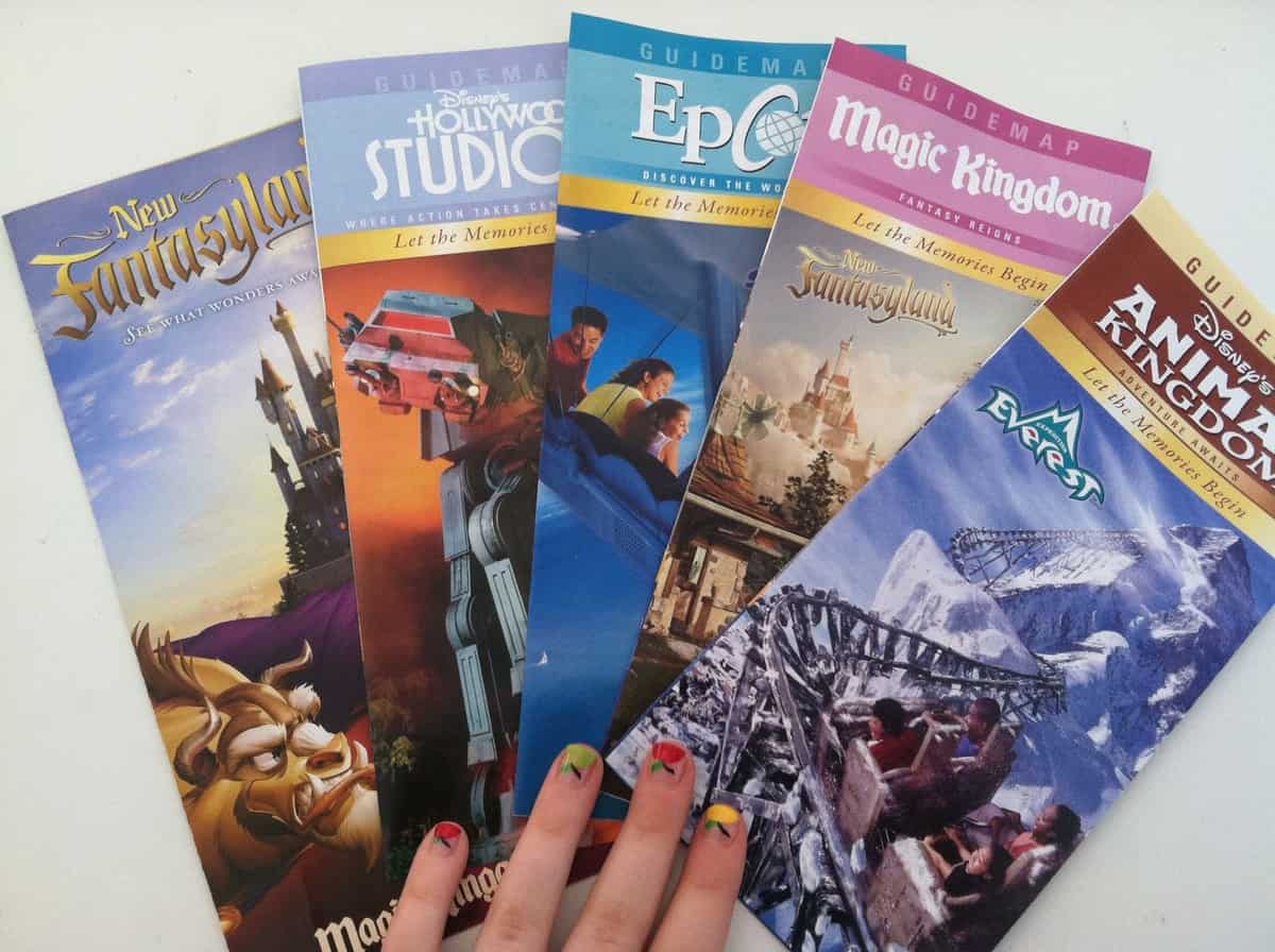 A fan showing off vibrant nails holds five Disney World park maps, ready for adventure across Magic Kingdom, EPCOT, Studios & Animal Kingdom.