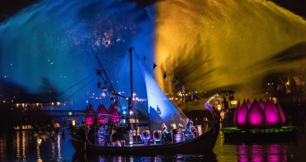 Nighttime spectacle at Animal Kingdom: dazzling fountains, vibrant lights, performers, boats, and glowing lotus floats on the lake.