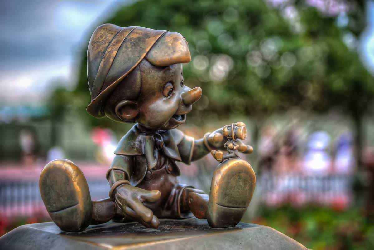 Pinocchio bronze statue holding Jiminy Cricket at Magic Kingdom, with a dreamy park backdrop—an iconic Disney photo spot.