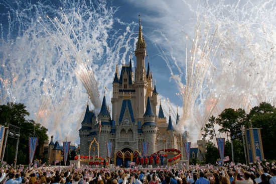 Fireworks light up Cinderella Castle as park guests gather to celebrate under clear blue skies at Magic Kingdom, Walt Disney World.
