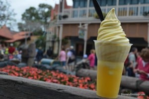 Pineapple Dole Whip soft serve with a spoon, enjoyed at Disney World amid bustling crowds and vibrant flowers—a fan-favorite treat.
