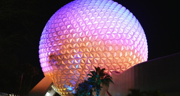 Spaceship Earth glows in vibrant purple, pink, and orange at night amid palm trees—a classic Epcot nighttime photo spot.
