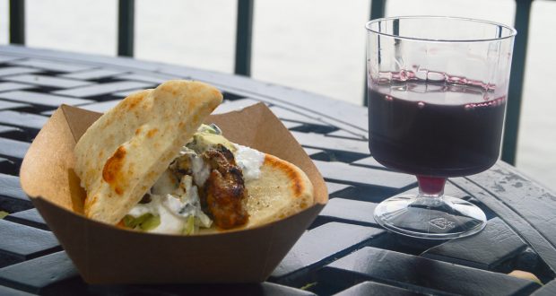 Gyro in a cardboard tray paired with red wine on a black table at Epcot, ready for Disney fans to savor during their visit.