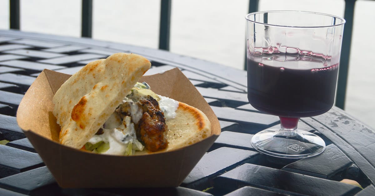 Gyro in a cardboard tray paired with red wine on a black table at Epcot, ready for Disney fans to savor during their visit.