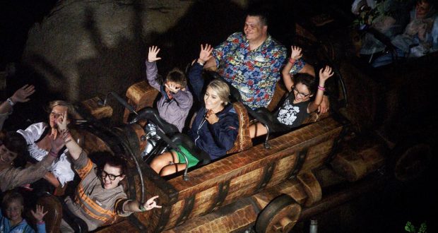 Guests throw their hands up and laugh on a wooden coaster, soaking in nighttime thrills at Walt Disney World.