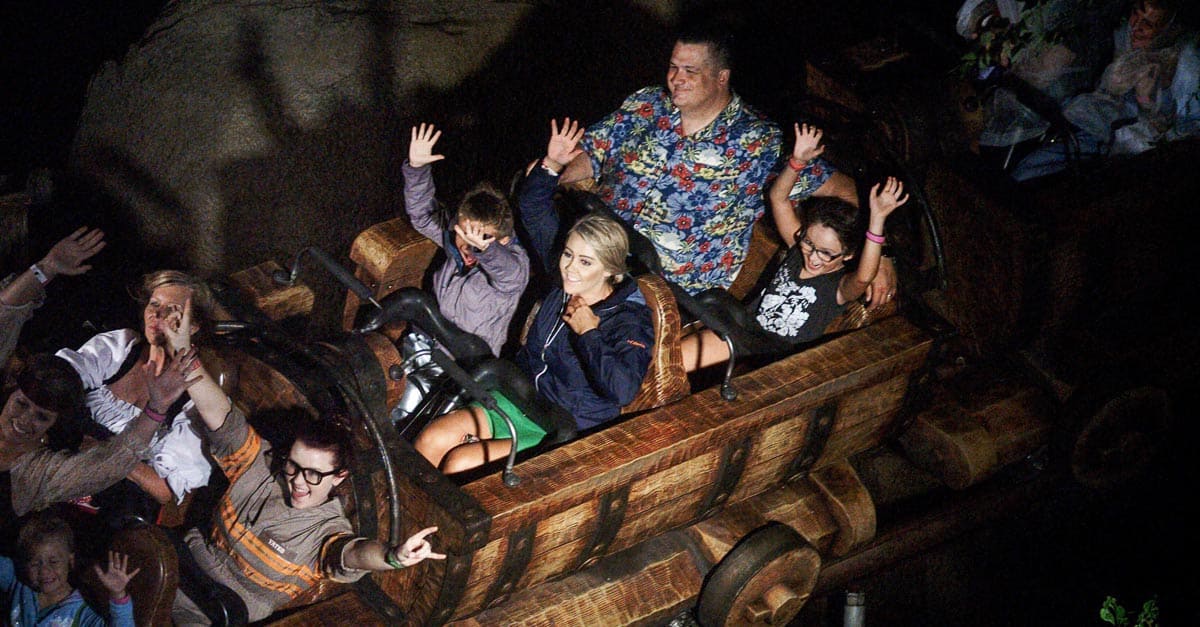 Guests throw their hands up and laugh on a wooden coaster, soaking in nighttime thrills at Walt Disney World.