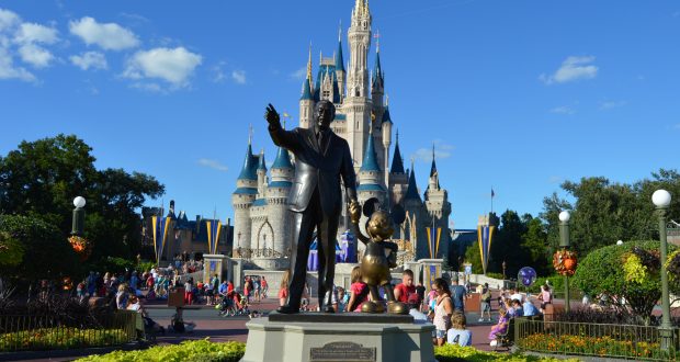 Walt Disney and Mickey Mouse statue in front of Cinderella Castle at Disney World, crowds enjoying a sunny, magical park day.
