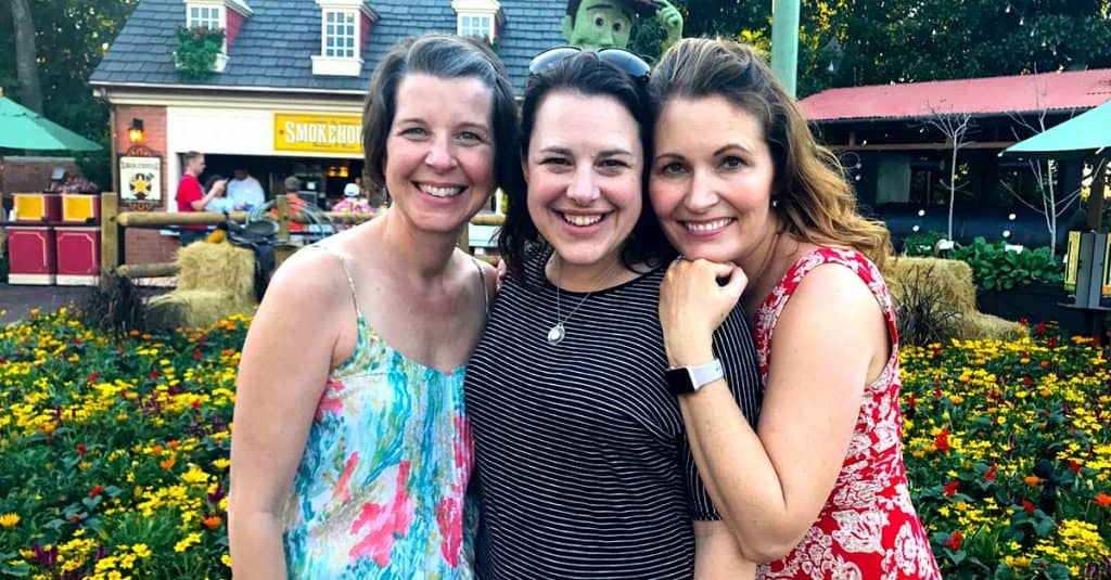 Three friends pose and smile in front of vibrant blooms, excitedly planning their next magical Walt Disney World adventure.