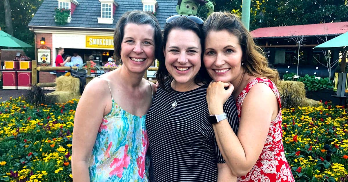 Three friends pose and smile in front of vibrant blooms, excitedly planning their next magical Walt Disney World adventure.
