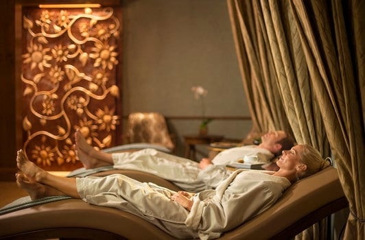 Guests unwind on lounge chairs in a tranquil Disney resort spa, surrounded by warm lighting and elegant décor after park adventures.
