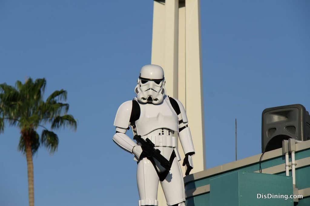 A stormtrooper stands atop a rooftop by a palm tree and tower at Disney's Hollywood Studios, possibly during attraction downtime.