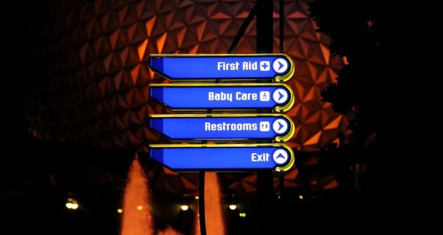 Glowing sign by Epcot’s geodesic dome points to first aid, baby care, restrooms, and exit—perfect for Disney World emergencies.