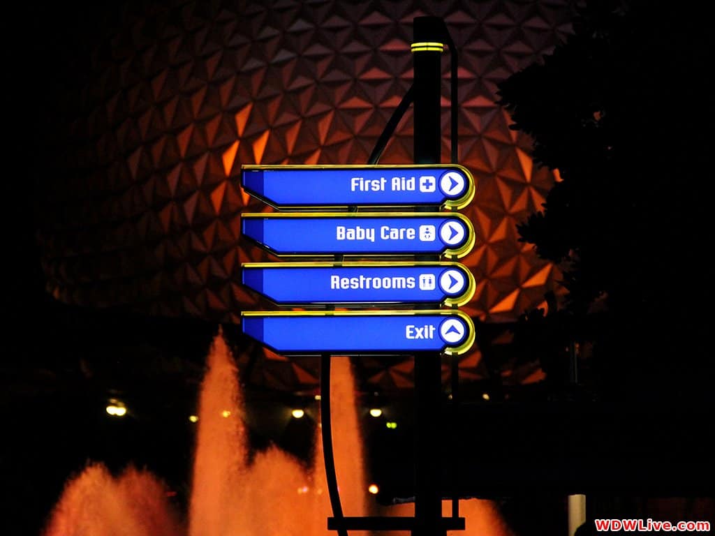 Glowing sign by Epcot’s geodesic dome points to first aid, baby care, restrooms, and exit—perfect for Disney World emergencies.