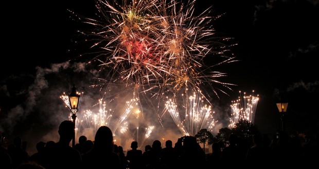 Guests at Magic Kingdom marvel as vibrant fireworks burst over Main Street, framed by glowing lamplights and leafy treetops.