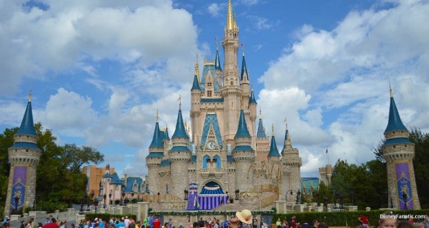 Guests fill the plaza before Disney World's iconic Cinderella Castle, its blue rooftops and gold spires gleaming beneath a bright sky.