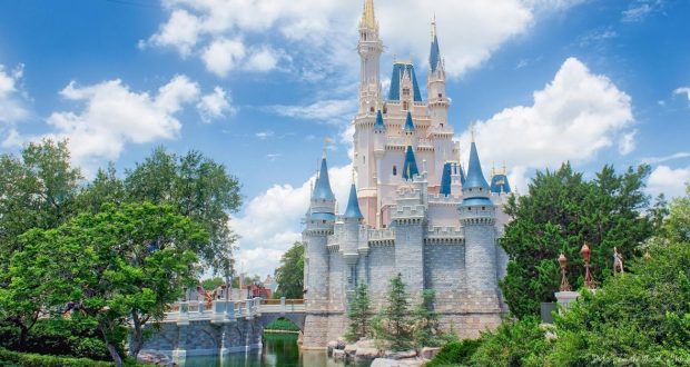 Cinderella Castle with iconic blue spires, surrounded by lush greenery and water, gleaming beneath a vibrant Magic Kingdom sky.