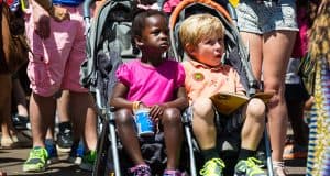 Two kids ride together in a double stroller at Disney World, surrounded by crowds—ideal for families planning park visits.