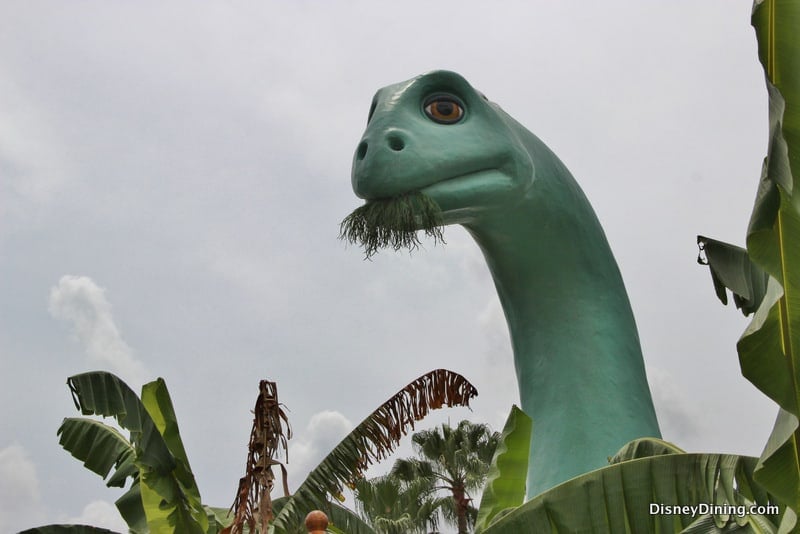 Gertie the Dinosaur statue munching foliage, surrounded by palms beneath cloudy skies at Disney’s Hollywood Studios.