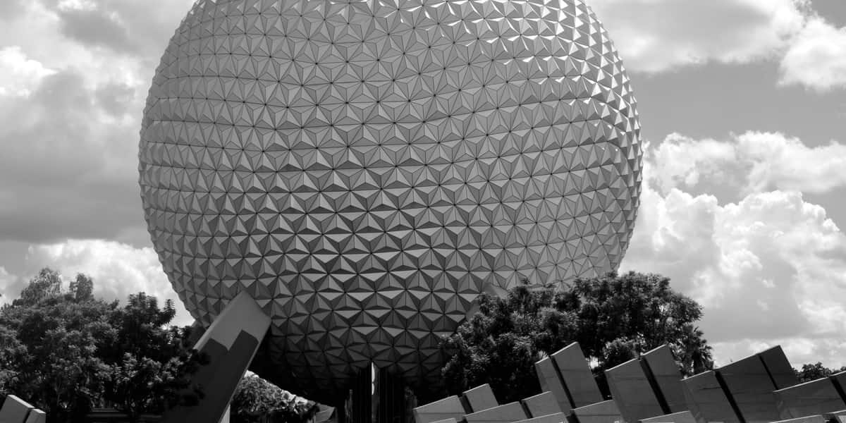 Spaceship Earth at Epcot in classic black and white, framed by lush trees and drifting clouds at Walt Disney World.