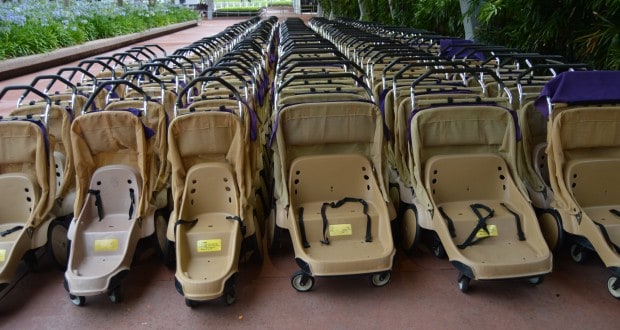 Neatly lined tan double strollers on a walkway near lush greenery—ready for families exploring Disney parks with little ones.