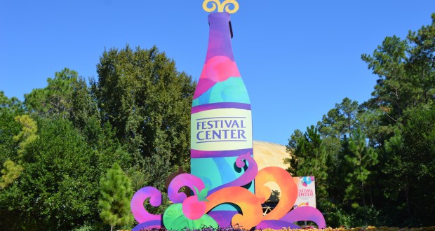 Festival Center’s bottle-shaped sign pops amid lush greenery and festive décor at Epcot Food & Wine 2015 as guests explore global menus.