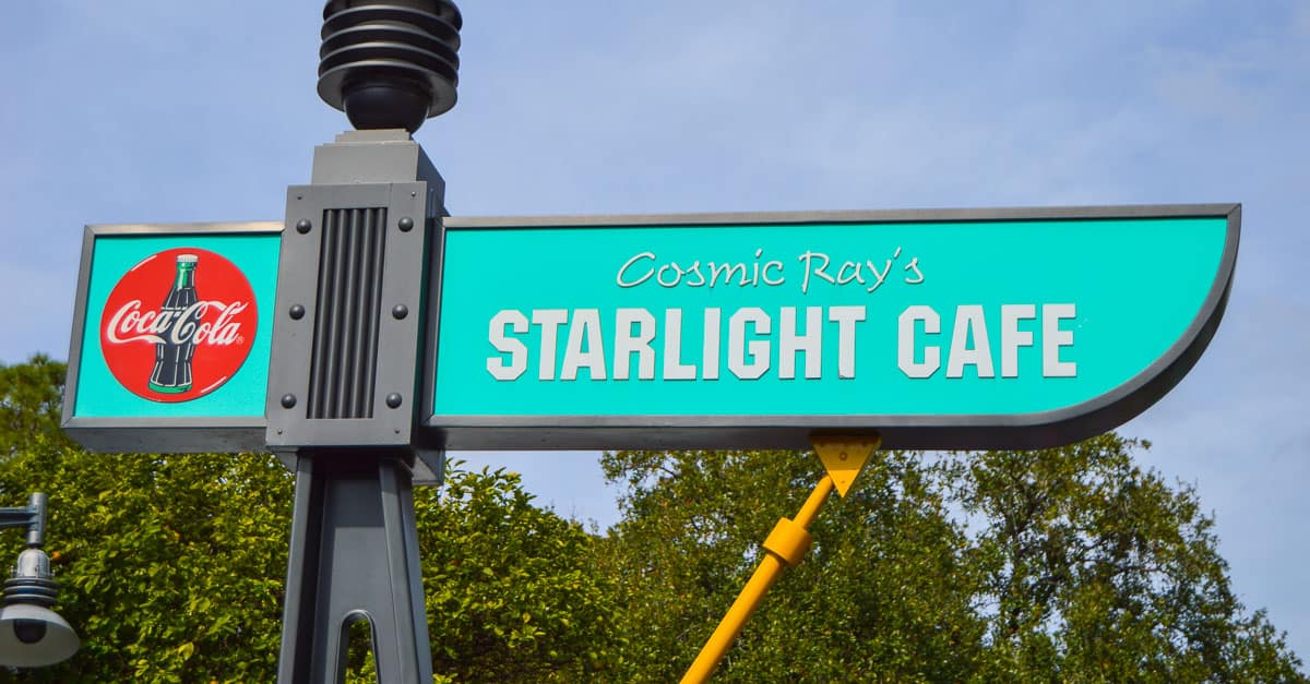 Cosmic Ray’s Starlight Cafe sign in turquoise with Coca-Cola logo, set among trees and sky, a classic Disney World eatery.